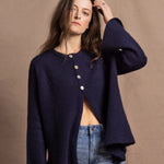 A woman wears a pure cashmere oversized cardigan with 4 buttons at the top in Navy Blue over a pair of jeans