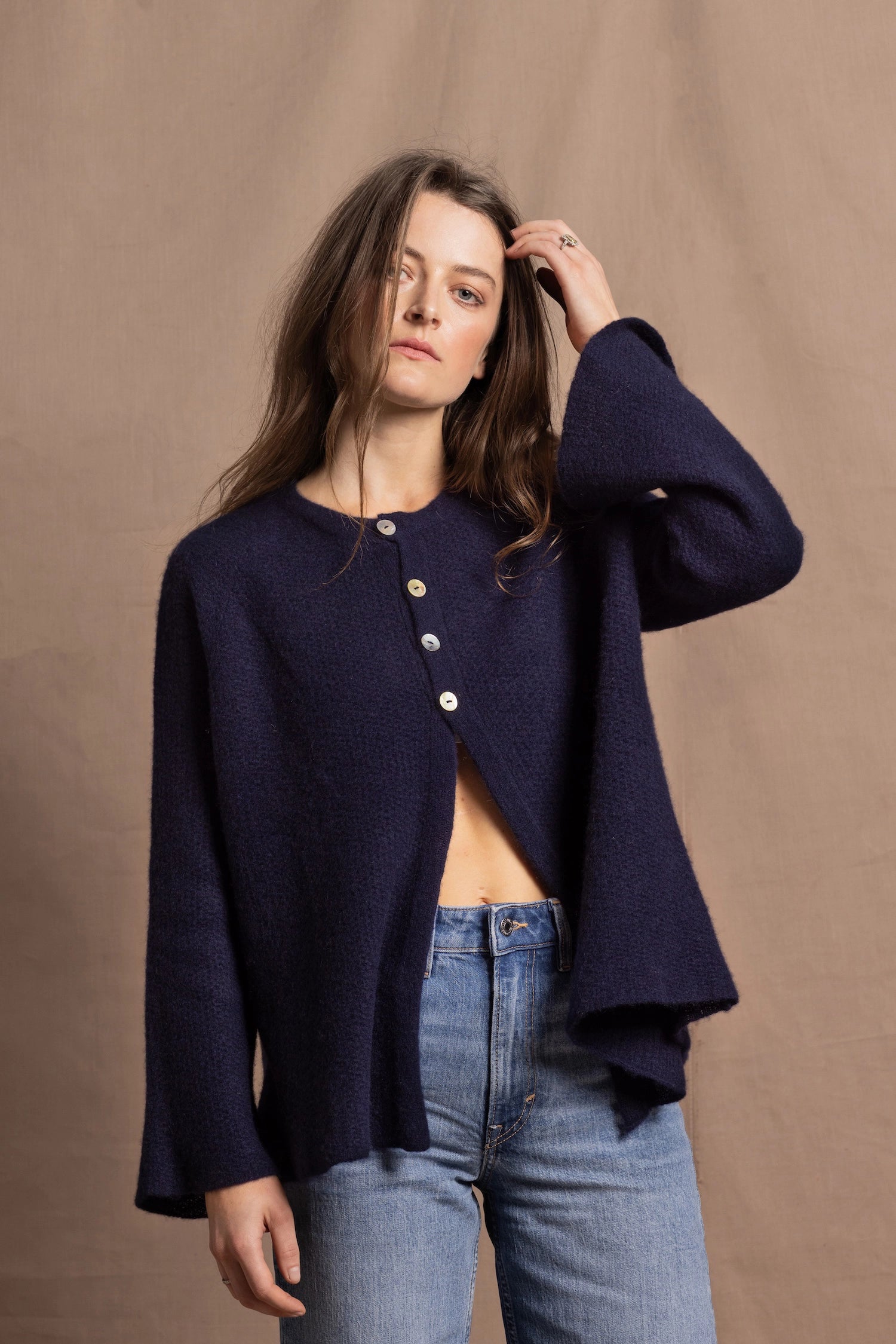 A woman wears a pure cashmere oversized cardigan with 4 buttons at the top in Navy Blue over a pair of jeans