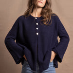 A woman wears a pure cashmere oversized cardigan with 4 buttons at the top in Navy Blue over a pair of jeans