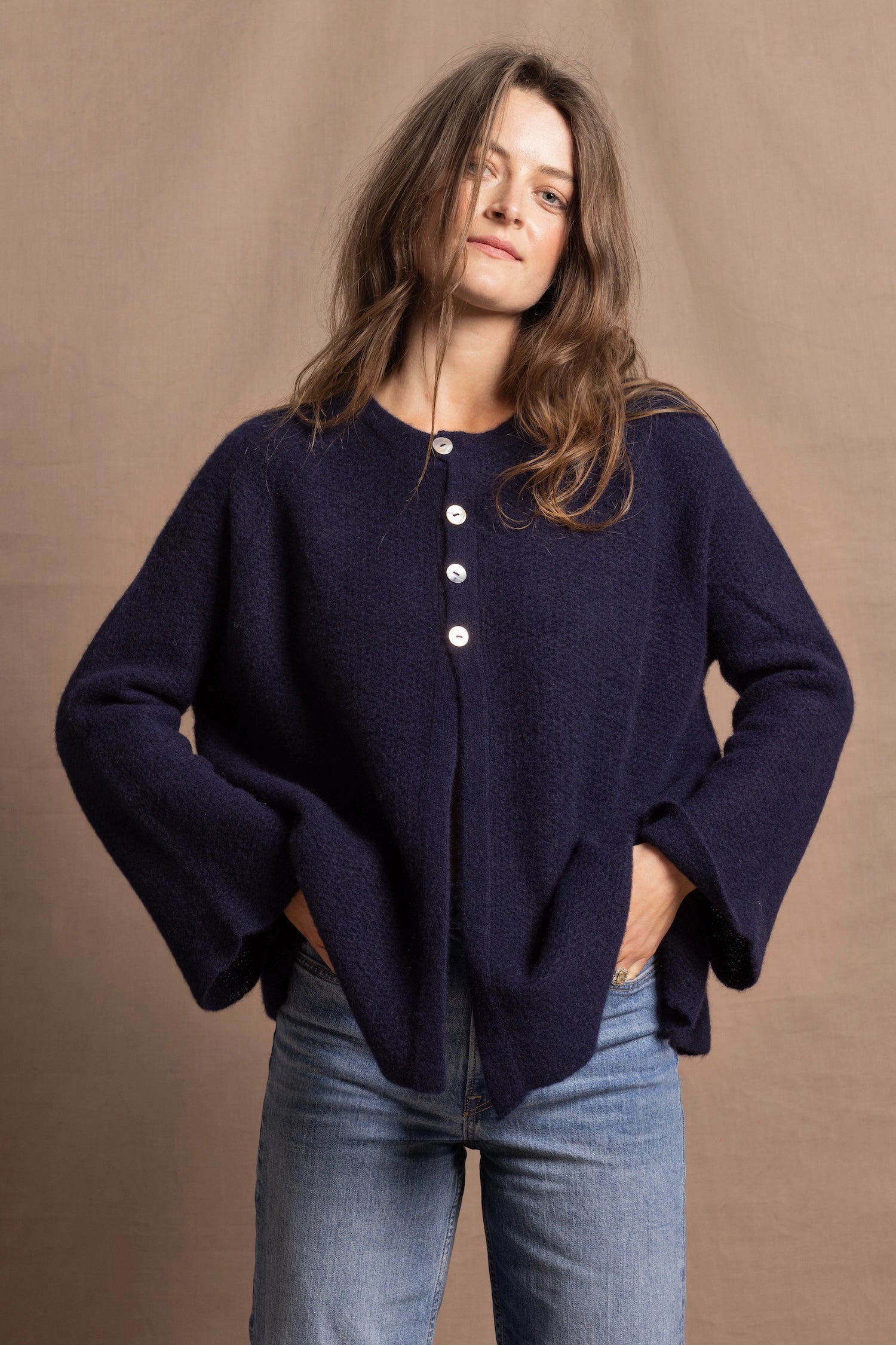 A woman wears a pure cashmere oversized cardigan with 4 buttons at the top in Navy Blue over a pair of jeans