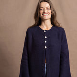 A woman wears a pure cashmere oversized cardigan with 4 buttons at the top in Navy Blue over a pair of jeans