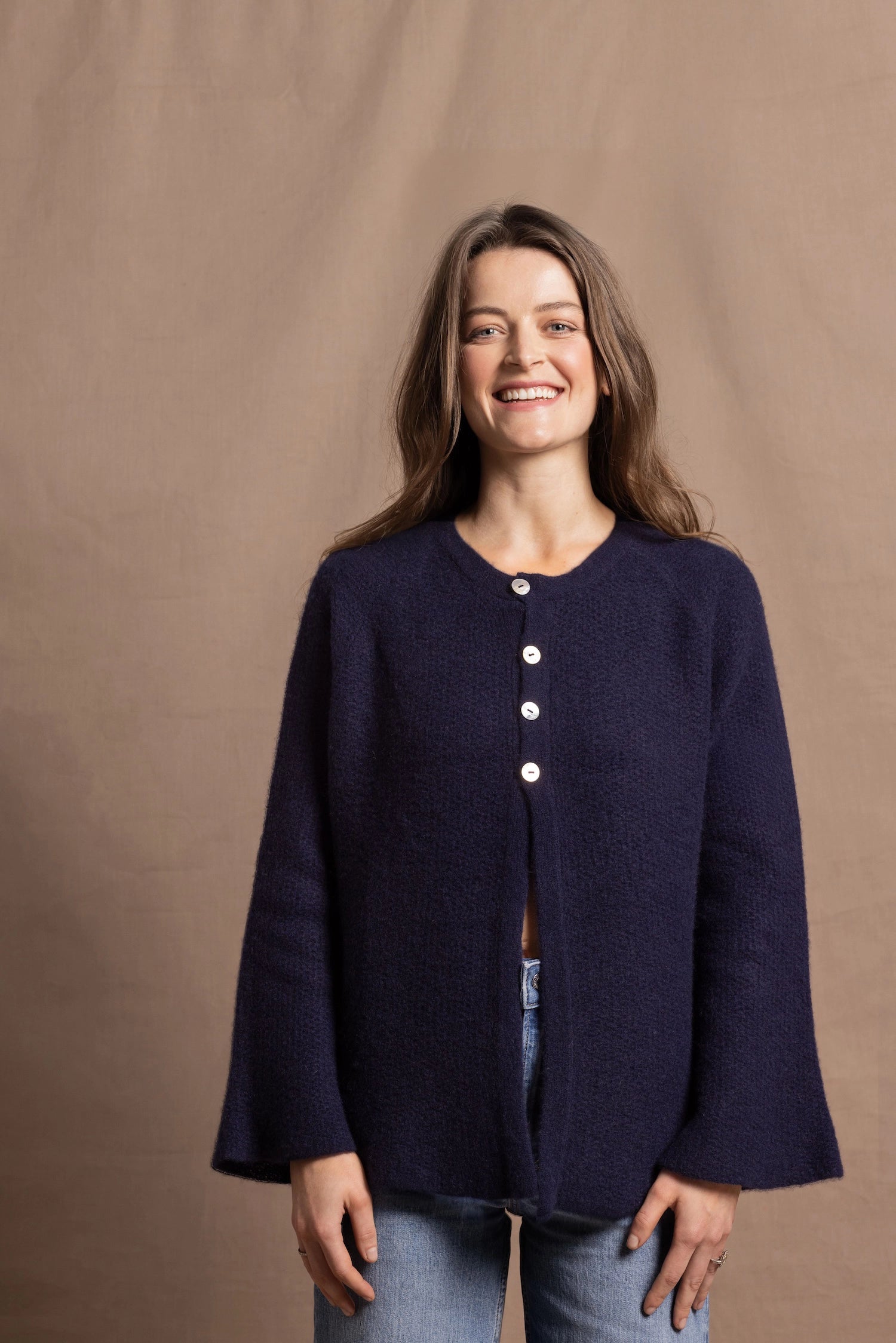 A woman wears a pure cashmere oversized cardigan with 4 buttons at the top in Navy Blue over a pair of jeans