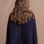 A woman wears a pure cashmere oversized cardigan with 4 buttons at the top in Navy Blue over a pair of jeans