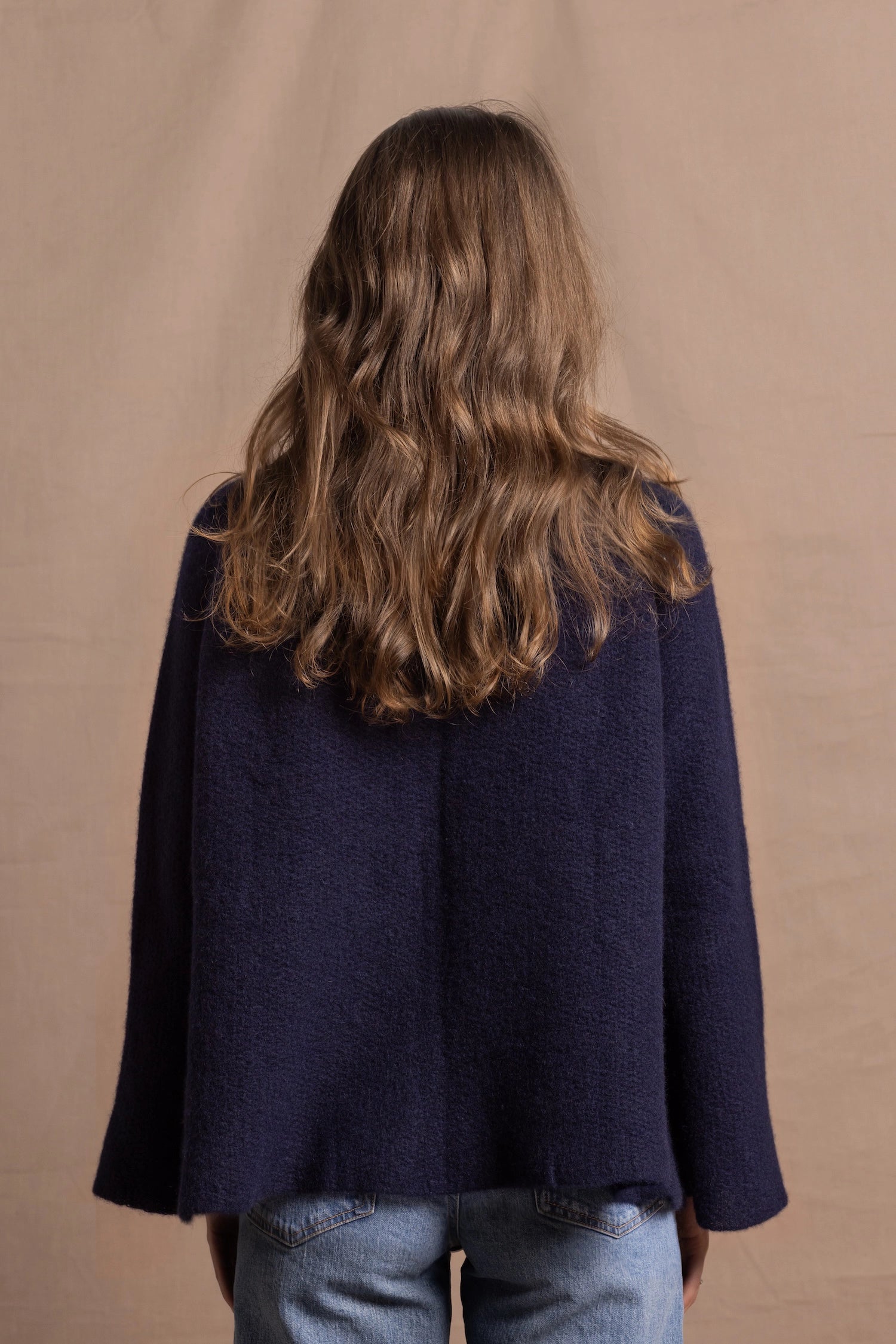 A woman wears a pure cashmere oversized cardigan with 4 buttons at the top in Navy Blue over a pair of jeans