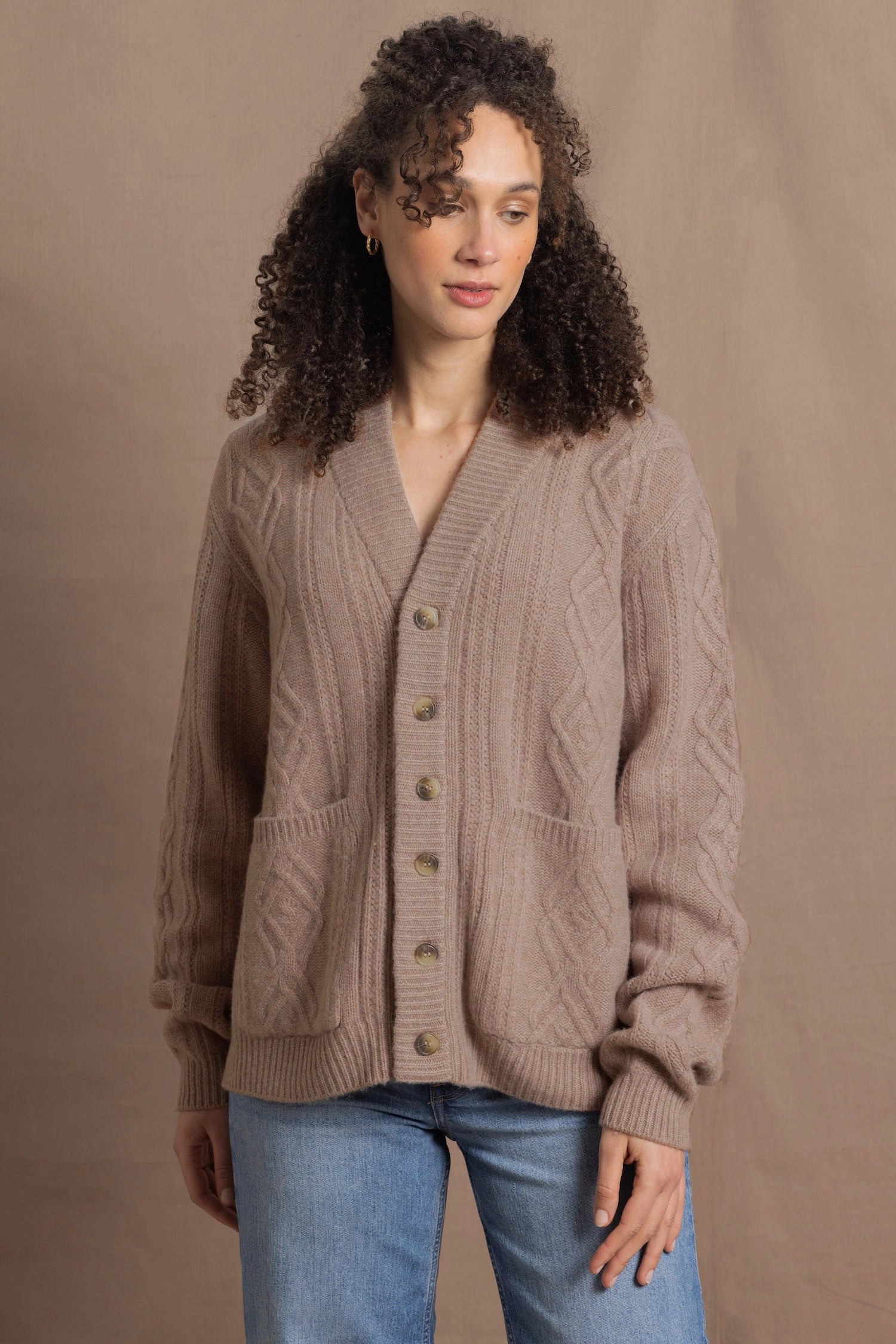 a woman wears a taupe coloured cashmere aran cardigan sweater with horn buttons