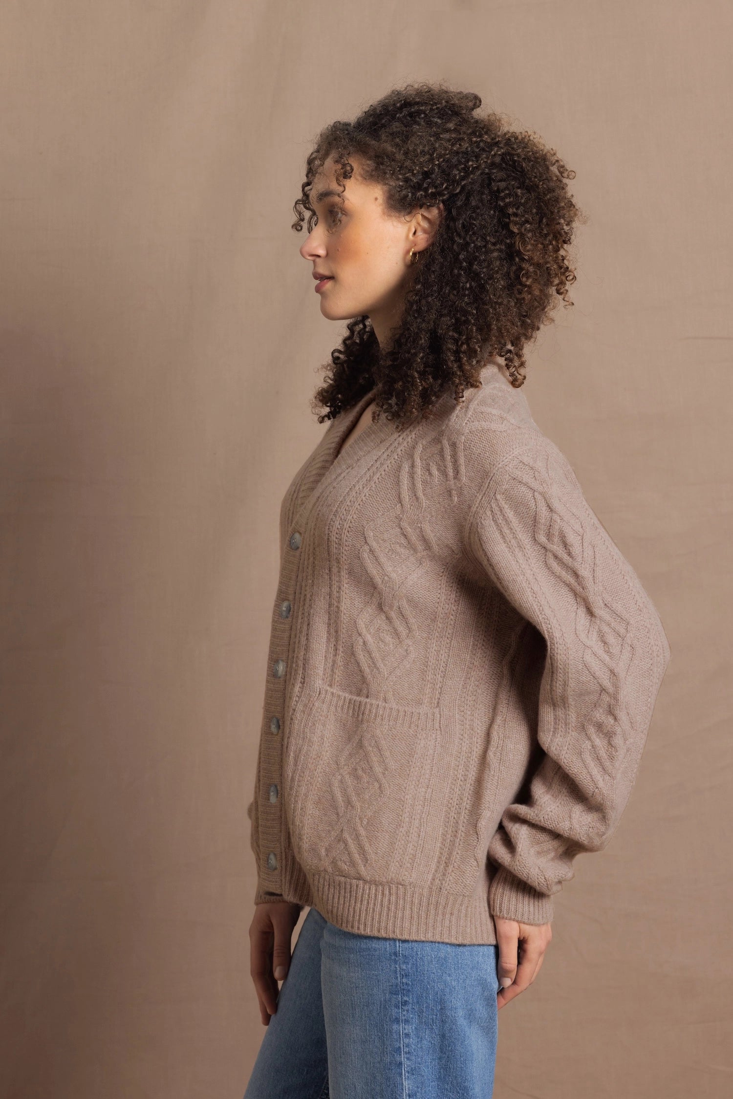 a woman wears a taupe coloured cashmere aran cardigan sweater with horn buttons