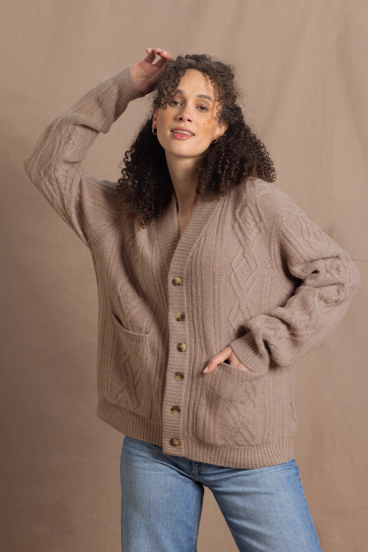 a woman wears a taupe coloured cashmere aran cardigan sweater with horn buttons