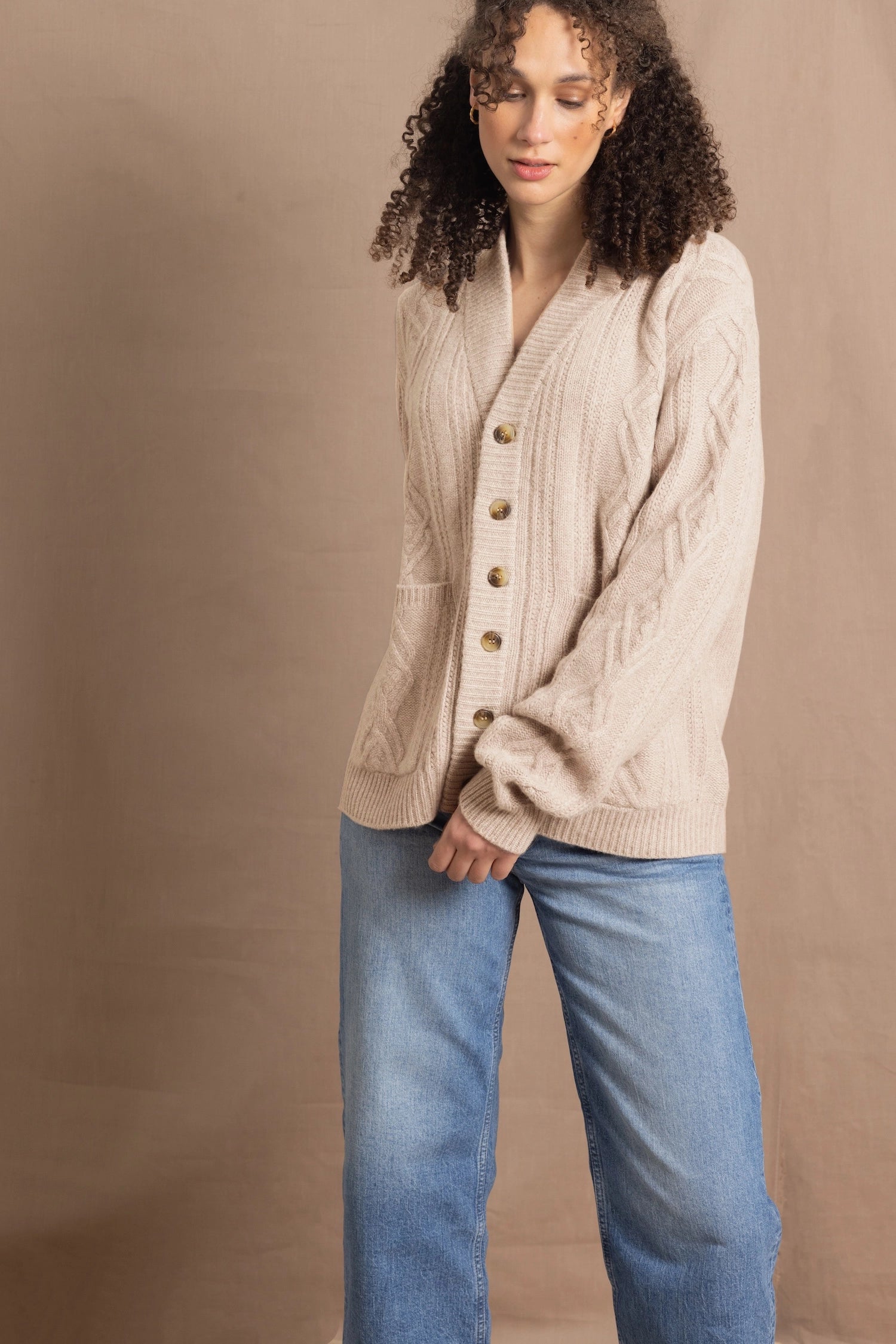a woman wears a beige coloured cashmere aran cardigan sweater with horn buttons