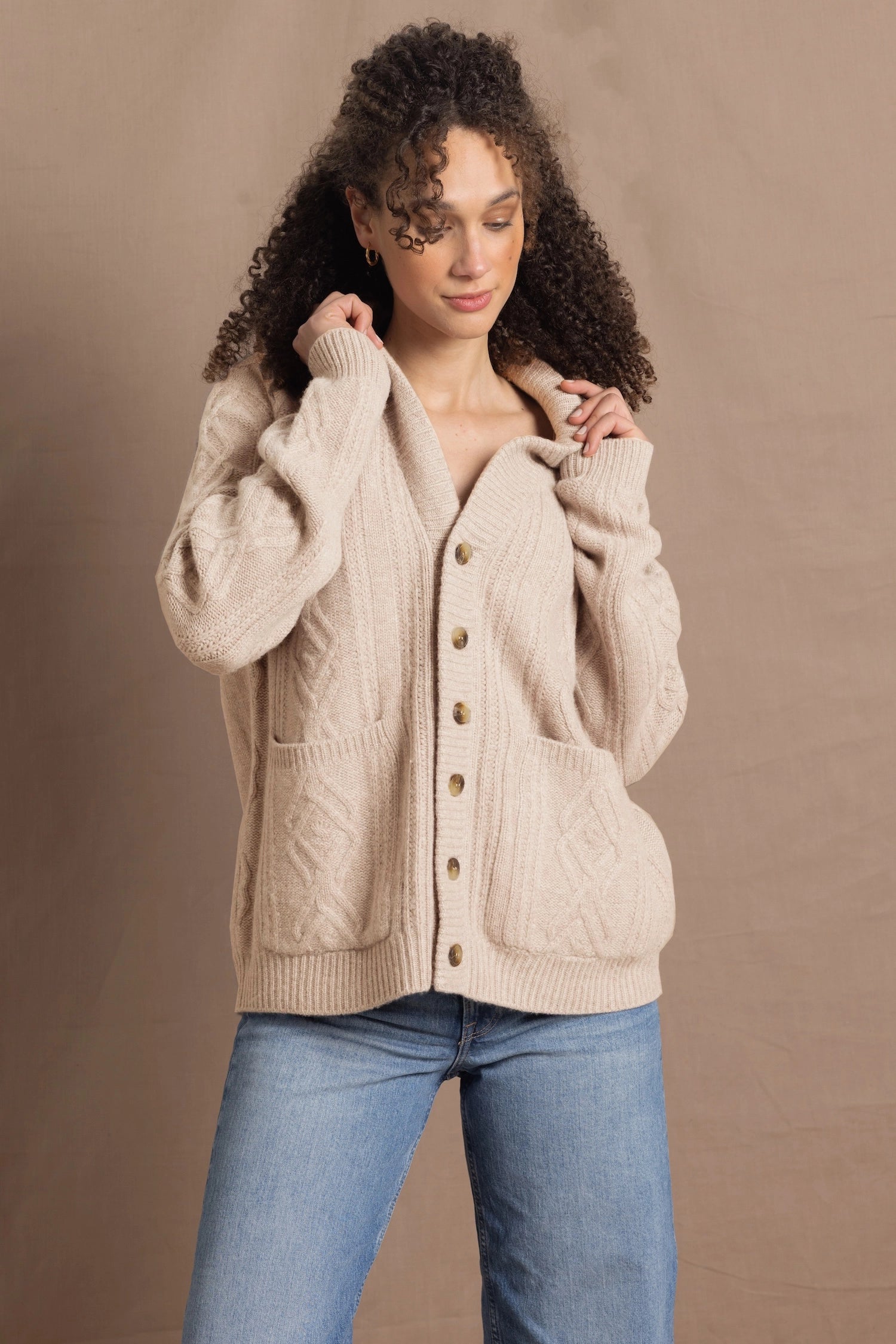 a woman wears a beige coloured cashmere aran cardigan sweater with horn buttons