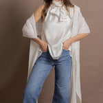 A woman wears a 100% silk pussybow sleeveless blouse in white with a pair of jeans and a matching cashmere lace shawl