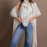 A woman wears a 100% silk pussybow sleeveless blouse in white with a pair of jeans and a matching cashmere lace shawl