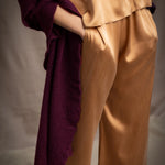 A woman wears a deep plum burgundy textured cashmere knit shawl draped over gold silk clothing by Irish brand Madigan Cashmere 
