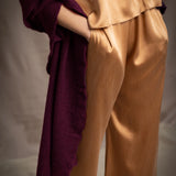 A woman wears a deep plum burgundy textured cashmere knit shawl draped over gold silk clothing by Irish brand Madigan Cashmere 