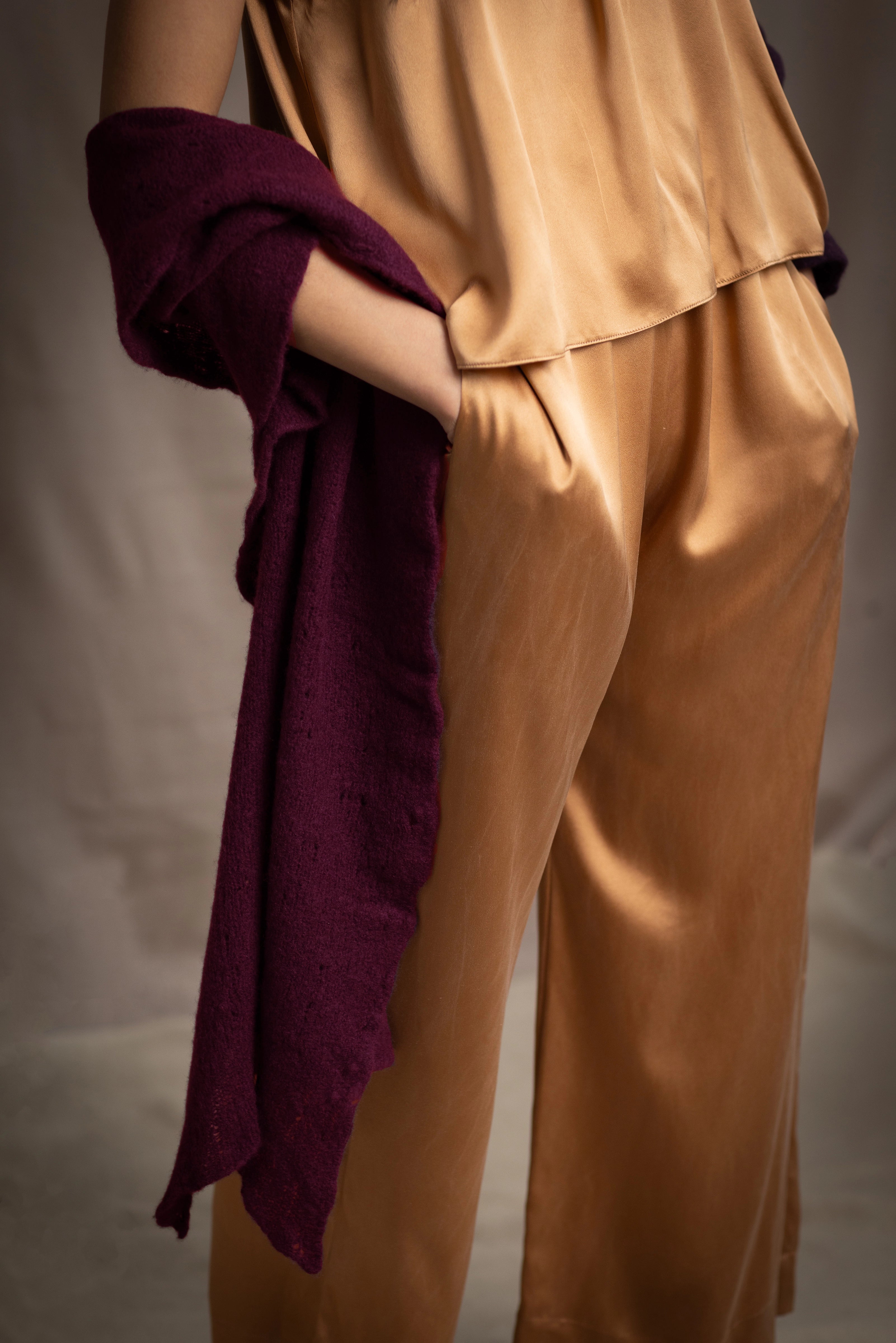 A woman wears a deep plum burgundy textured cashmere knit shawl draped over gold silk clothing by Irish brand Madigan Cashmere 