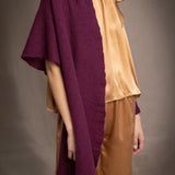 A woman wears a deep plum burgundy textured cashmere knit shawl draped over gold silk clothing by Irish brand Madigan Cashmere 