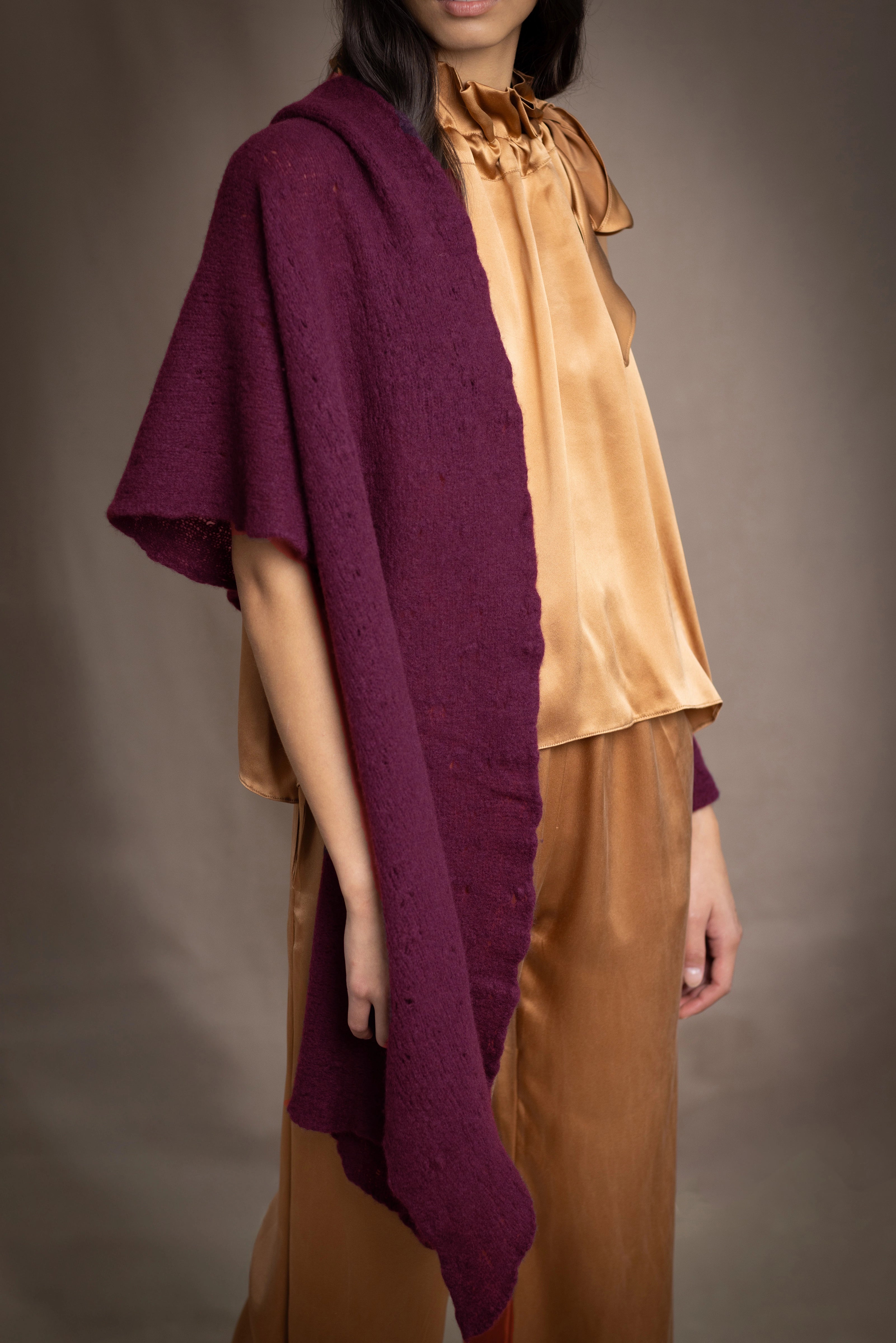 A woman wears a deep plum burgundy textured cashmere knit shawl draped over gold silk clothing by Irish brand Madigan Cashmere 