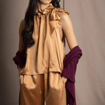 A woman wears a deep plum burgundy textured cashmere knit shawl draped over gold silk clothing by Irish brand Madigan Cashmere 