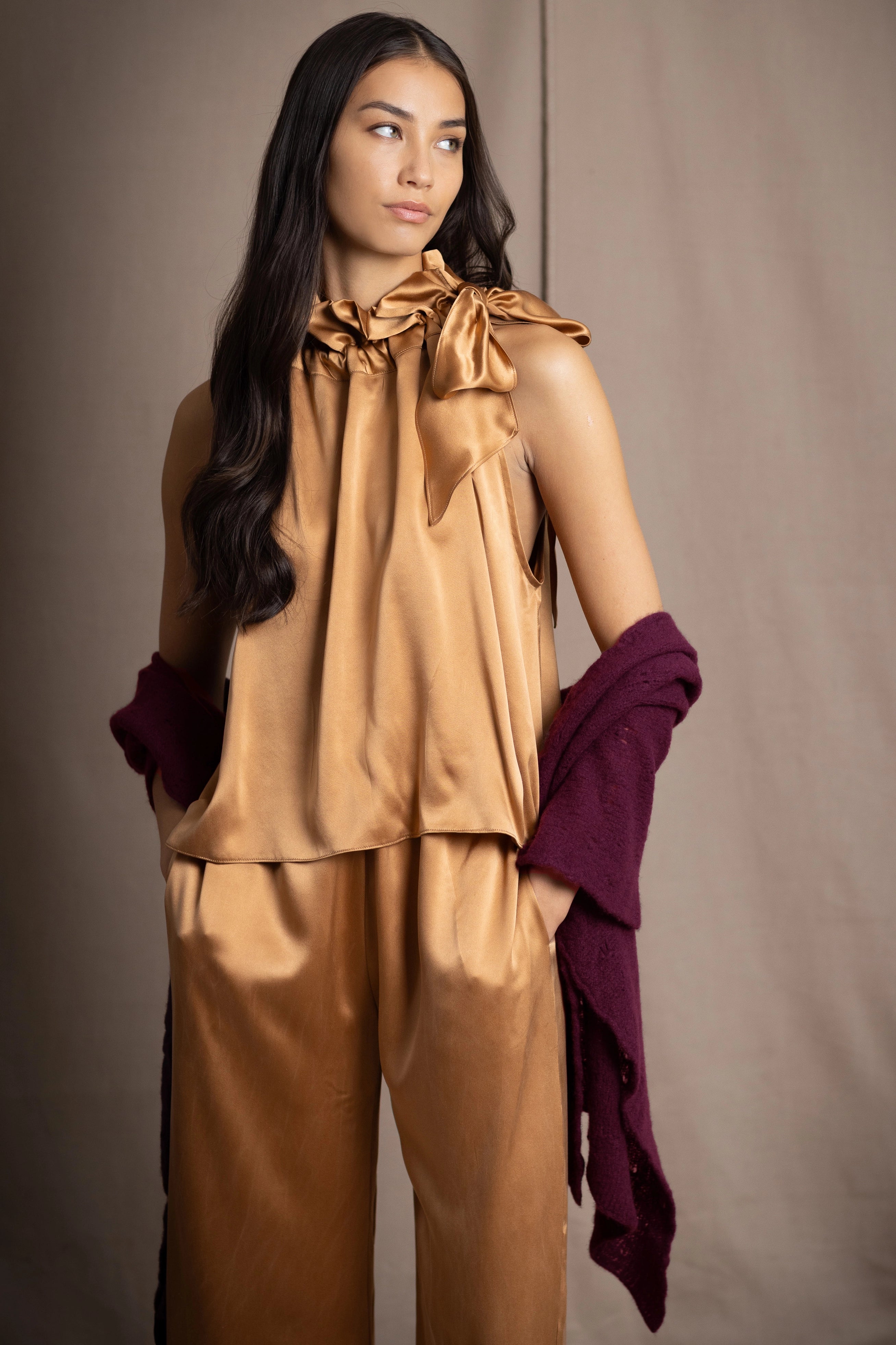 A woman wears a deep plum burgundy textured cashmere knit shawl draped over gold silk clothing by Irish brand Madigan Cashmere 