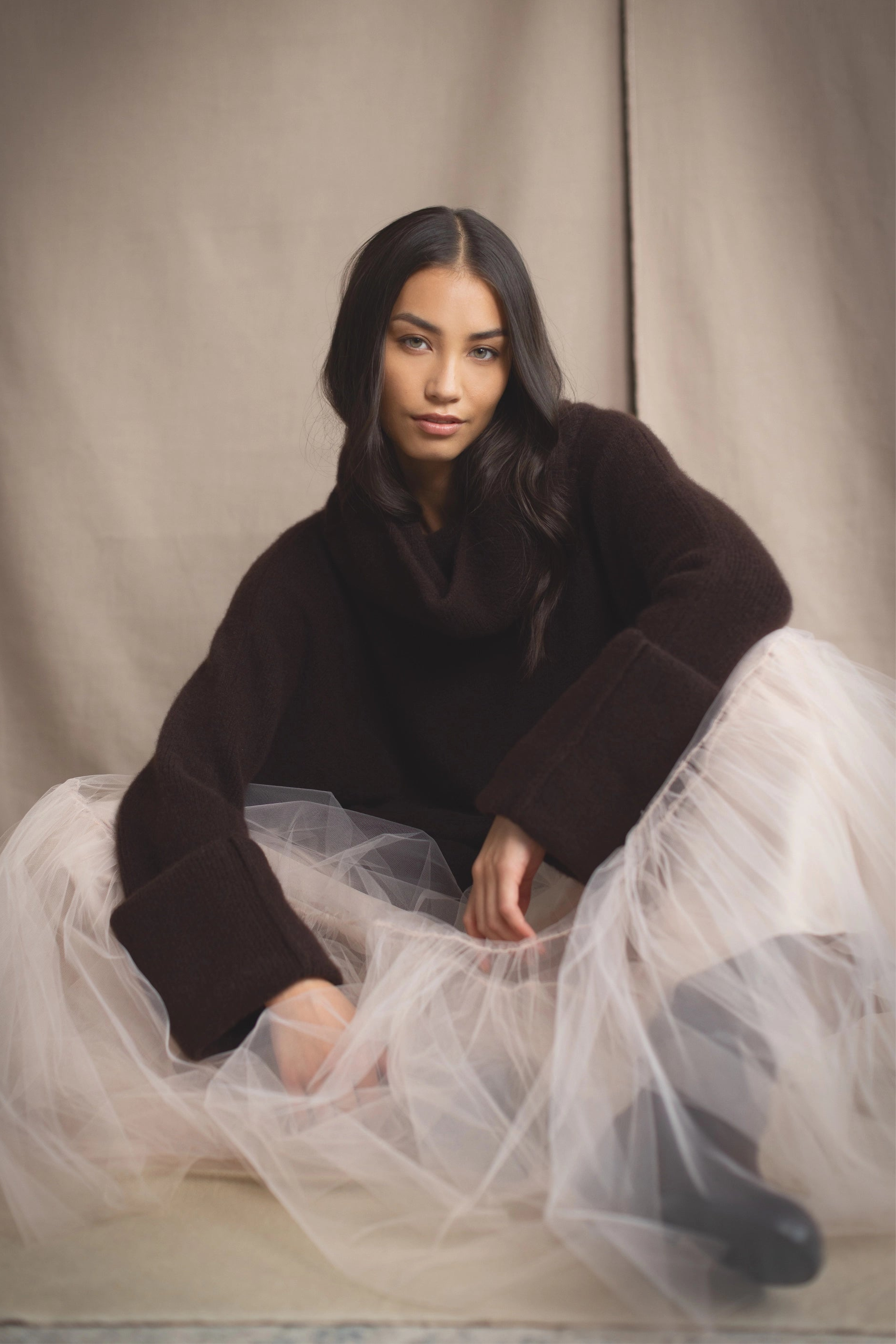 Woman sitting wearing a dark brown cashmere sweater and pale pink tulle skirt 