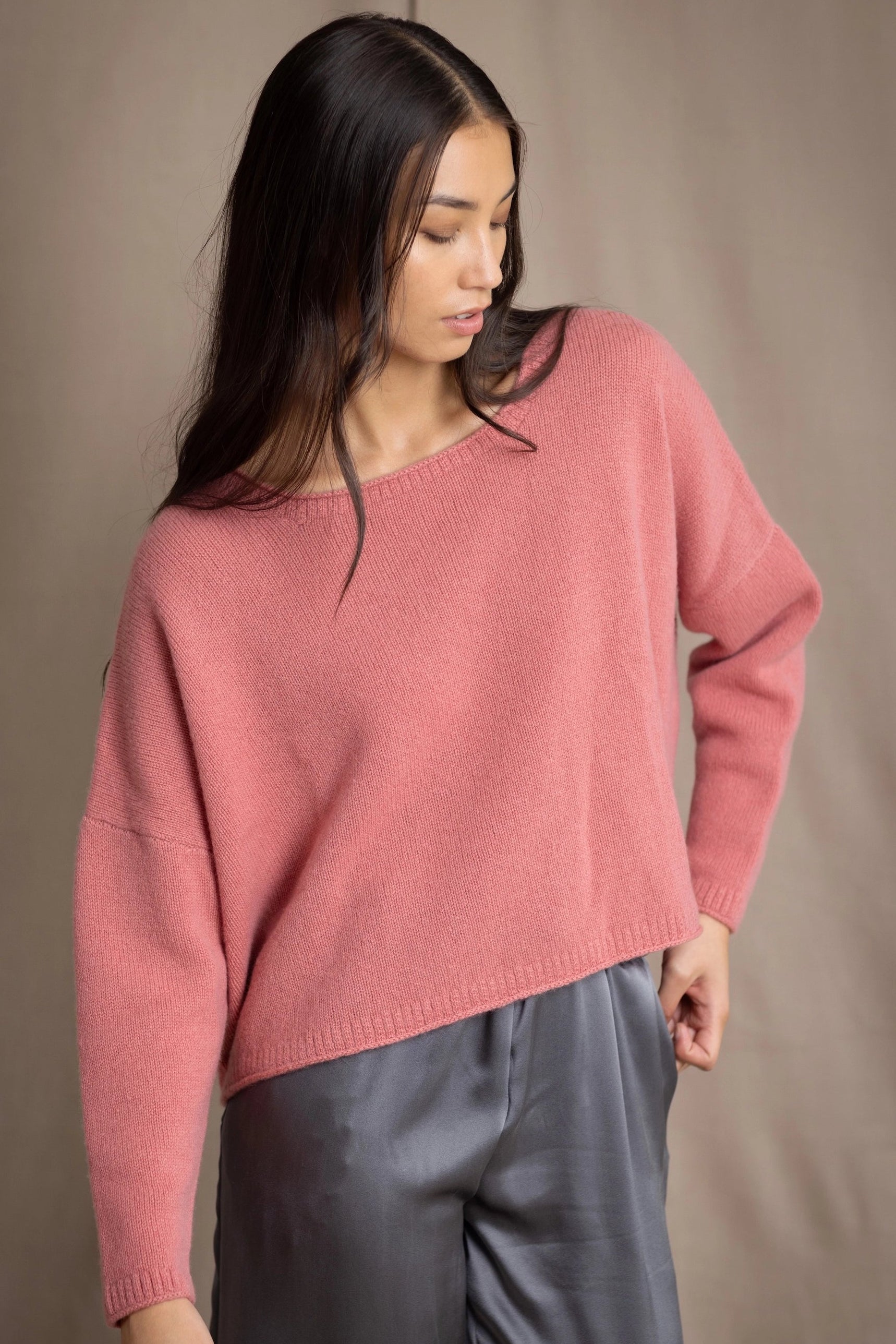 A woman wearing a dusty rose pink cashmere sweater with a wide  neckline and long sleeves by Irish quiet luxury brand Madigan Cashmere