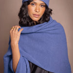 A woman modelling a matching cashmere beanie hat and shawl wrap in a medium blue