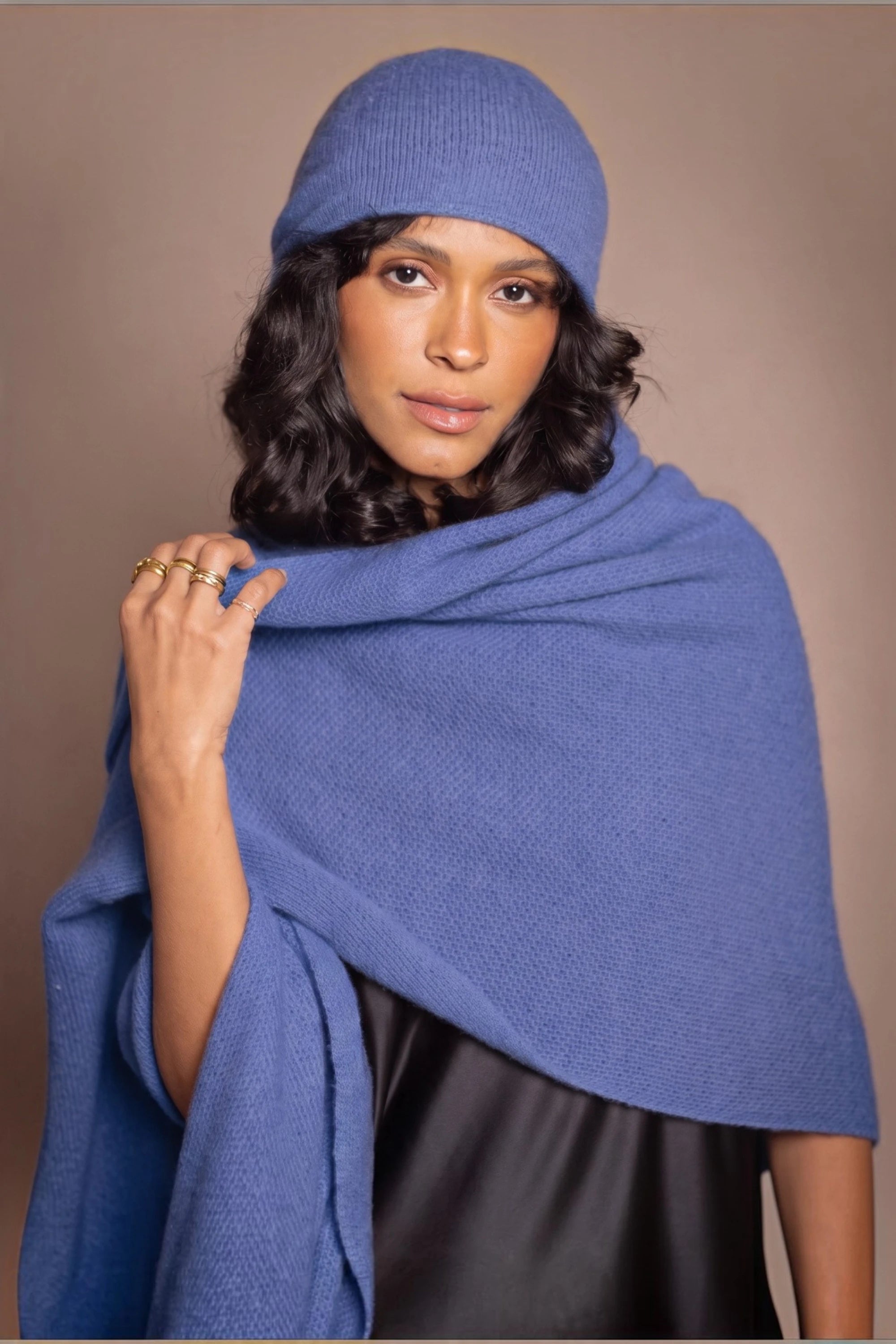 A woman modelling a matching cashmere beanie hat and shawl wrap in a medium blue
