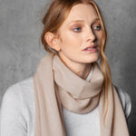 a lady wears a small cashmere scarf in a warm neutral beige colour