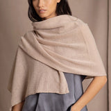 A woman wearing a beige cashmere wrap shawl draped over her shoulders by luxury Irish brand Madigan Cashmere