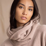 A woman wears a beige cashmere textured snood infinity scarf over beige cashmere sweater