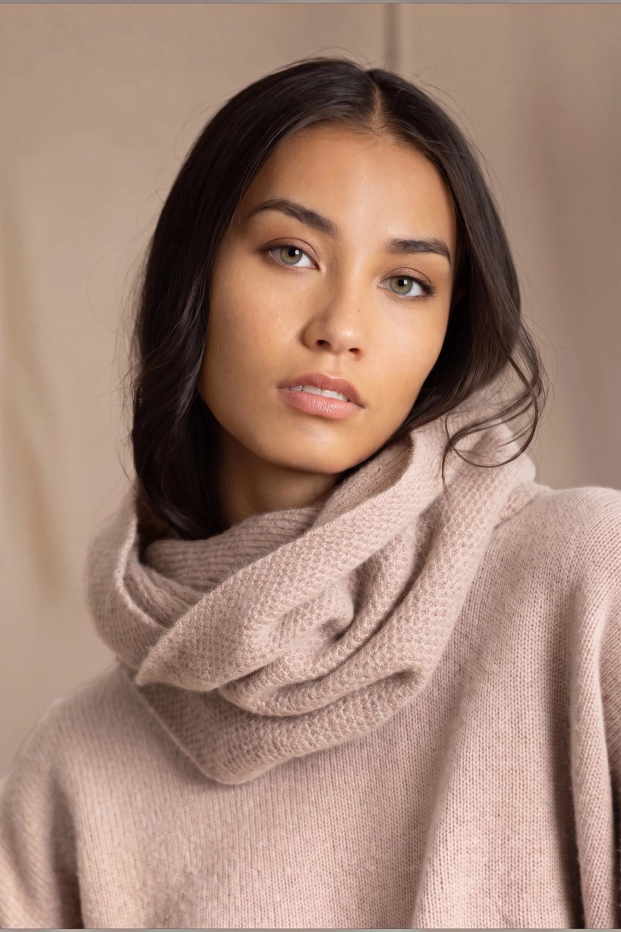 A woman wears a beige cashmere textured snood infinity scarf over beige cashmere sweater