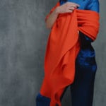 A lady wears a 100% cashmere wrap shawl in orange with a pure silk 3/4 sleeve blouse in teal with matching trousers