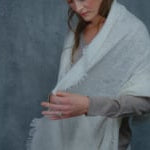a woman wears a thin, feather light cashmere wrap scarf in ivory over a summerweight cashmere sweater in taupe 