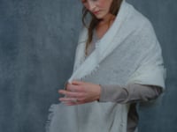 a woman wears a thin, feather light cashmere wrap scarf in ivory over a summerweight cashmere sweater in taupe 