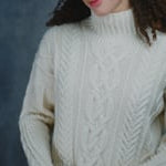 A woman wears a traditional Irish Aran Sweater made in 100% Cashmere and black silk skirt