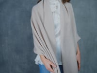 A woman wears a large cashmere shawl in beige over a white silk pussybow top