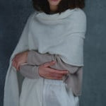 A woman wears a cropped cashmere sweater in beige with white silk shorts and matching white cashmere wrap