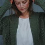 a woman wears a forest green cashmere aran cardigan sweater full of blackberry stitches