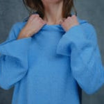 A woman wears a pure 100% cashmere hoodie sweater in blue with black silk shorts