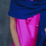 A woman wears a 100% silk pussy bow top in bright pink with matching trousers and a blue wrap shawl