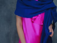 A woman wears a 100% silk pussy bow top in bright pink with matching trousers and a blue wrap shawl