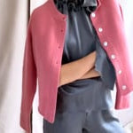 video of a woman wearing a cashmere cardigan  in dusty pink rose with mother of pearl buttons over dark grey silk top and trousers