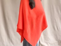 video of a woman wearing a cashmere cape in orange with matching cashmere beanie hat over grey silk skirt
