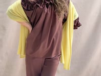 a video of a woman wearing a banana yellow cashmere wrap shawl over a ruffled silk blouse top in chocolate brown with matching trousers 