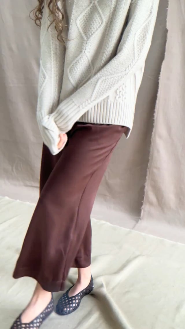 a video of a woman wearing a hand knit Irish 100% Cashmere Aran Sweater with Turtleneck in cream beige colour over chocolate brown silk trousers
