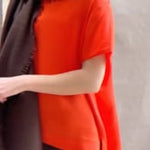 a video of a woman wearing a lightweight cashmere wrap shawl in chocolate brown over a silk tee in bright orange and chocolate brown silk trousers