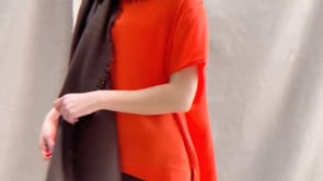 a video of a woman wearing a lightweight cashmere wrap shawl in chocolate brown over a silk tee in bright orange and chocolate brown silk trousers