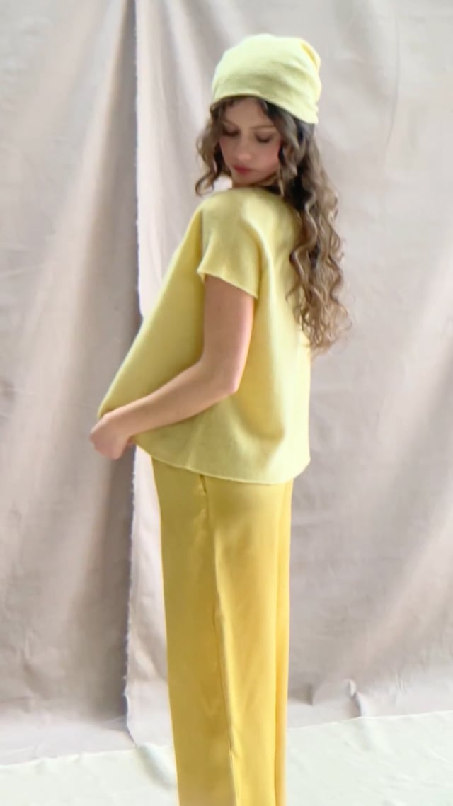 a video of a woman wearing a pure 100% cashmere tee sweater in butter yellow over silk trousers in butter yellow with a mathing cashmere beanie hat in butter yellow