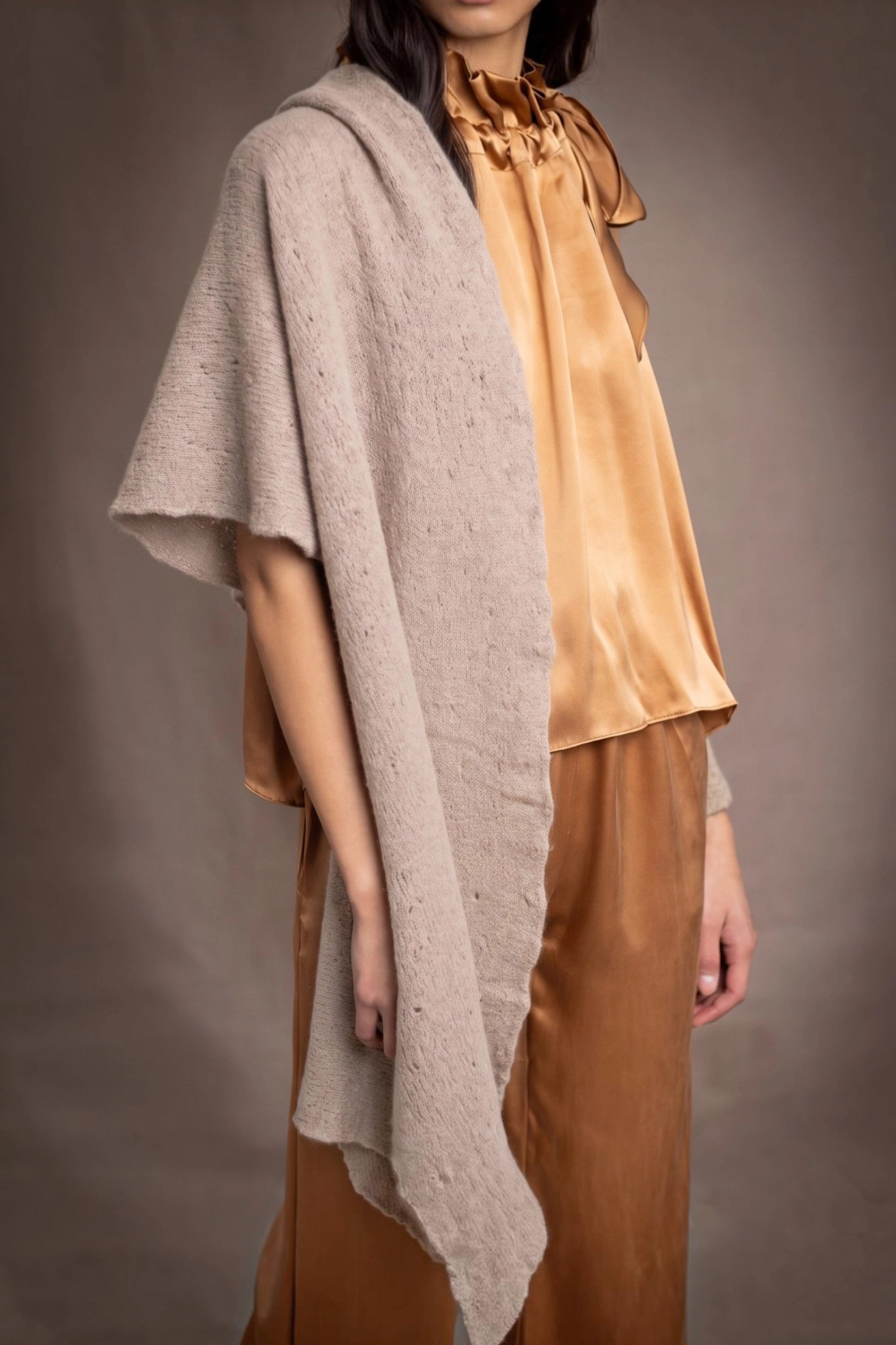A woman wears a beige cashmere lace textured wrap throw over bronze silk clothing by Irish brand Madigan Cashmere