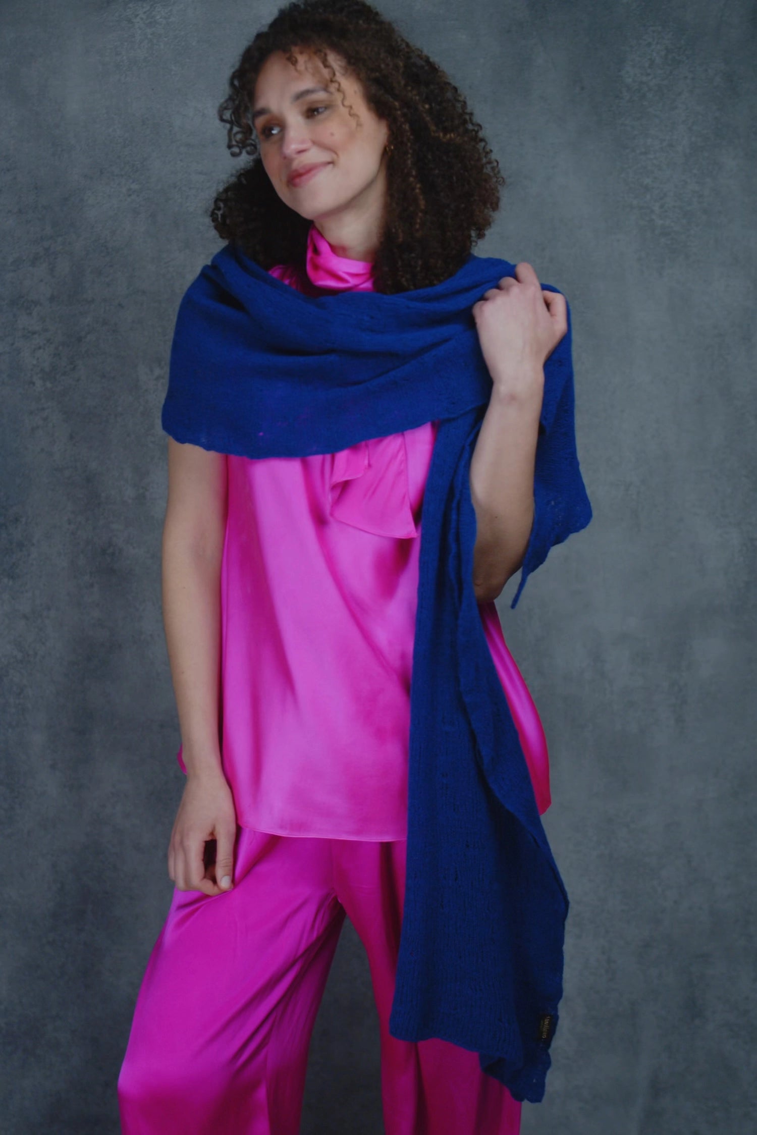 a woman wears a lace cashmere wrap shawl in indigo blue over her bright pink silk clothing