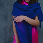 a woman wears a lace cashmere wrap shawl in indigo blue over her bright pink silk clothing